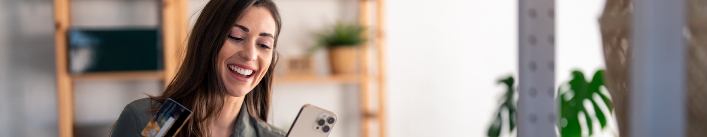 young woman holding a smart phone and debit card in a store with plants on the shelves